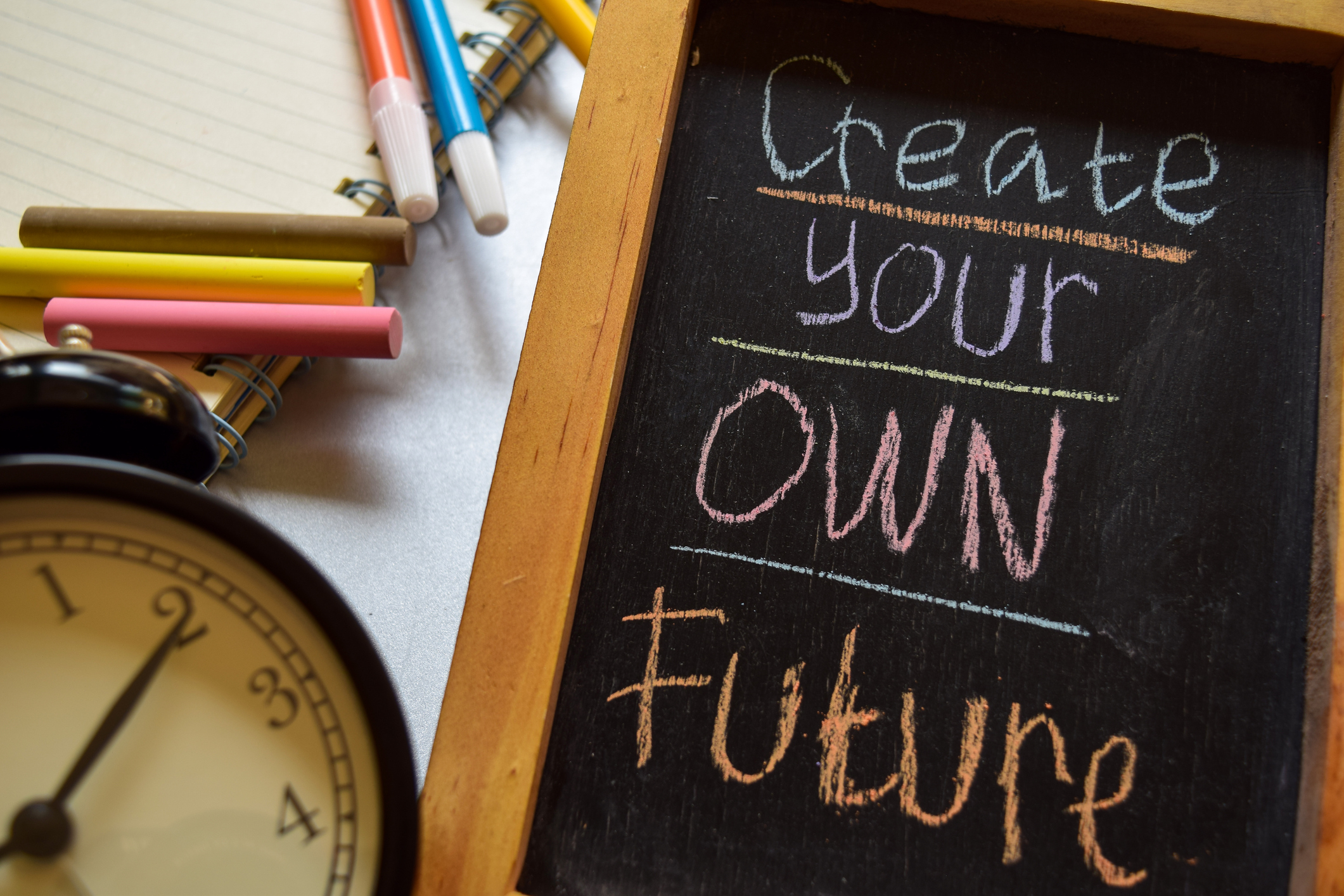 Create your own future on phrase colorful handwritten on chalkboard, alarm clock with motivation and education concepts.
